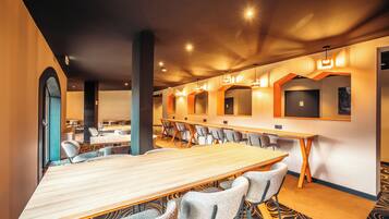 A conference room with a long table and multiple chairs, a high ceiling with recessed lighting, and a patterned carpet.