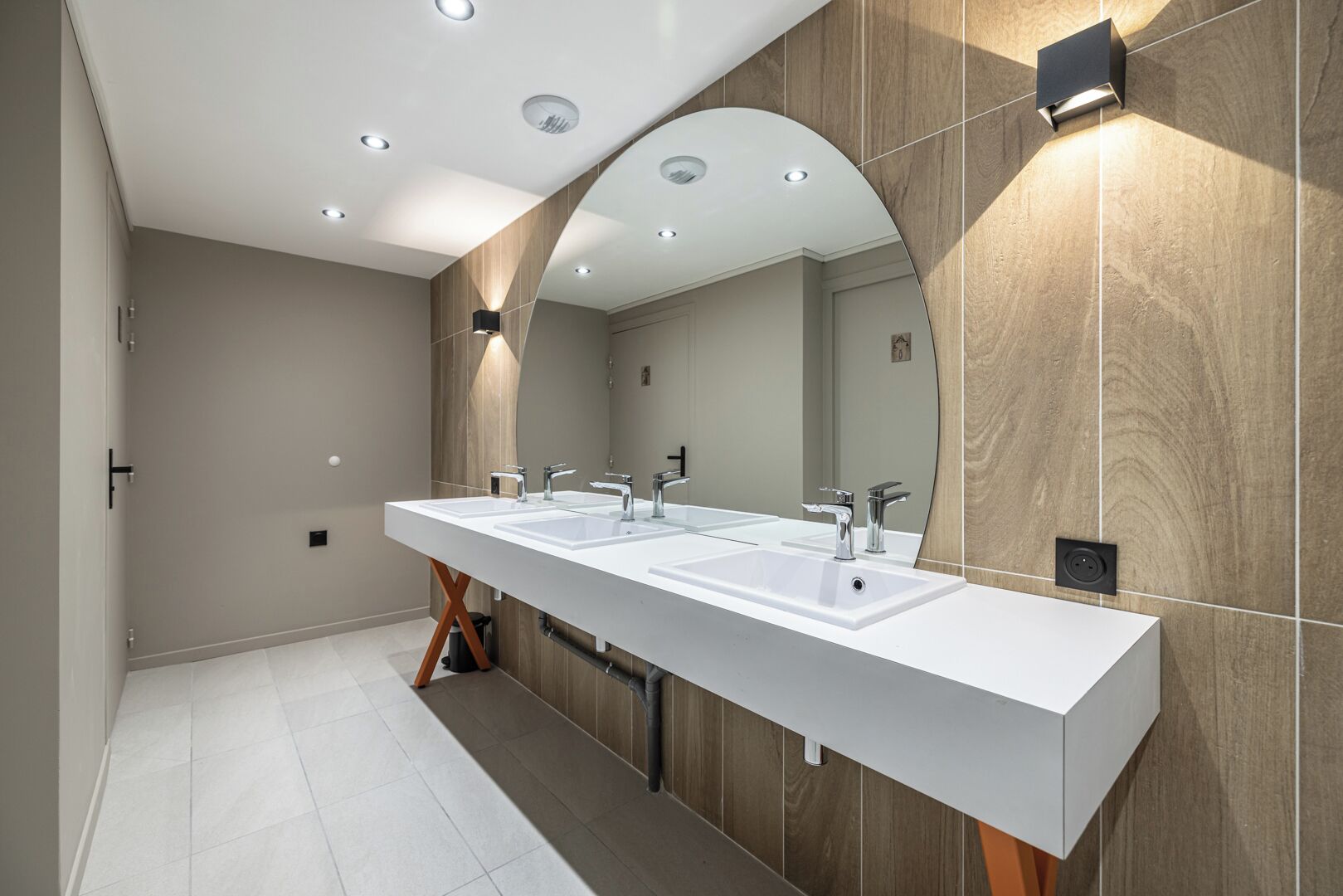 A modern bathroom with a long white sink, two mirrors, and recessed lighting.