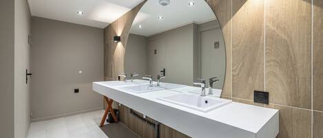 A modern bathroom with a long white sink, two mirrors, and recessed lighting.