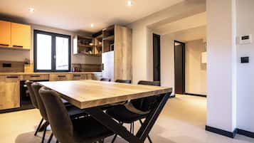 A modern kitchen with a wooden table and chairs, built-in shelves, and a large window.