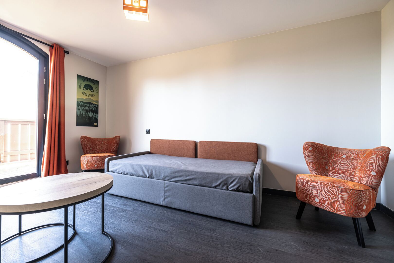 A compact room with a bed, a round table, and a patterned armchair.