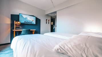 Habitación de hotel con dos camas, un escritorio con silla, un televisor montado en la pared y una puerta que da a otra habitación.