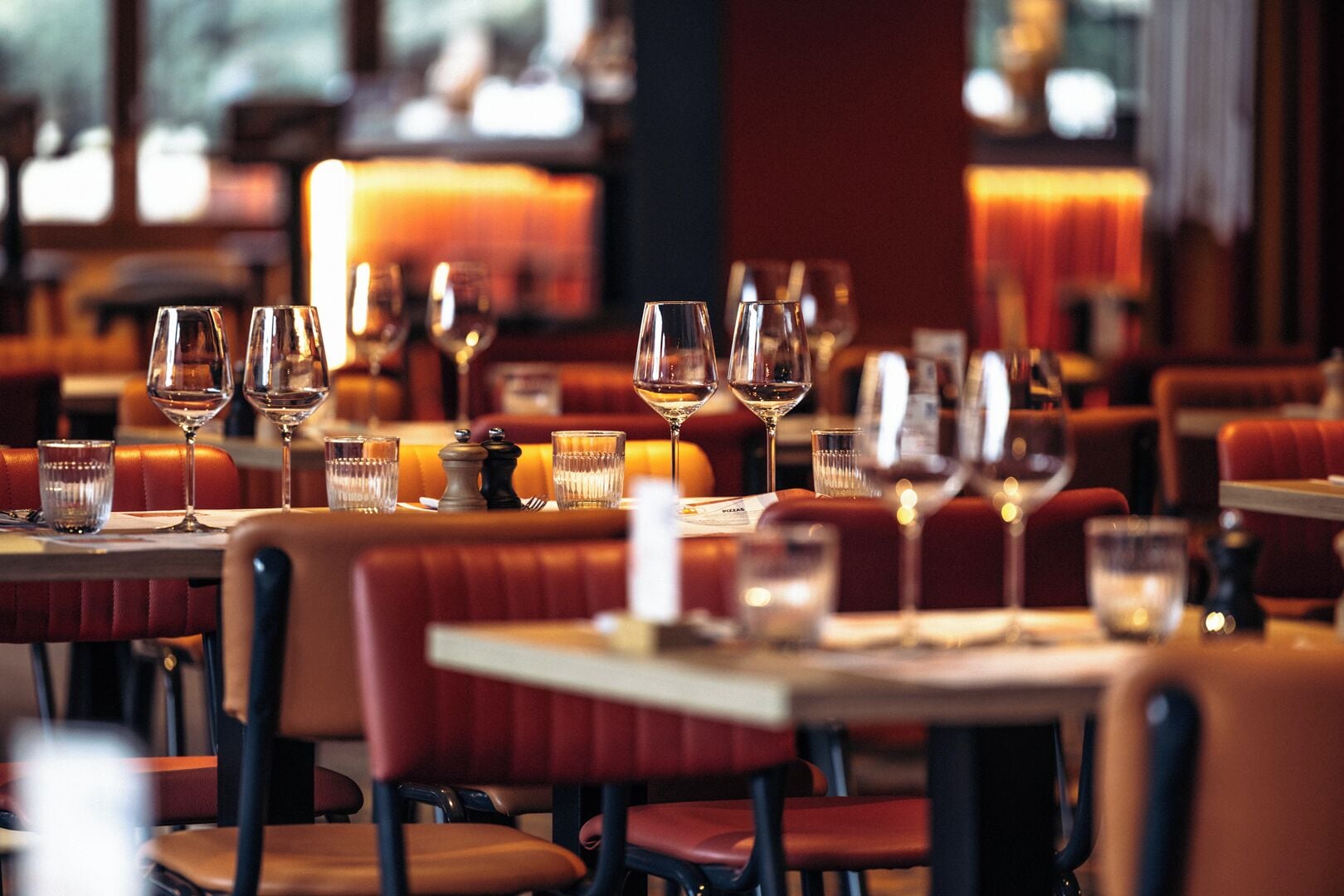 A restaurant interior with multiple tables and booths, each set with wine glasses and cutlery.