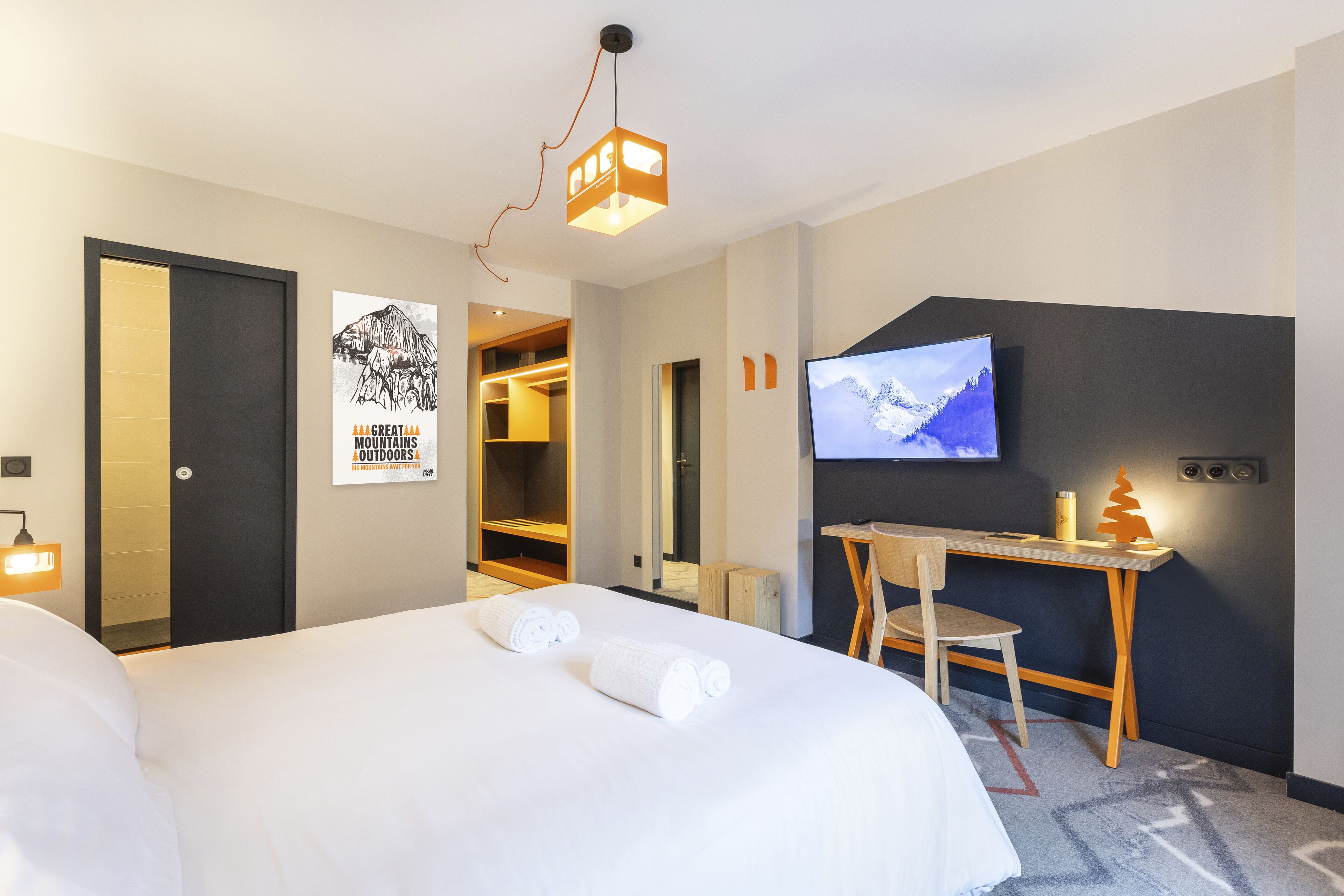 A hotel room with a bed, a desk, a TV, and a poster on the wall.