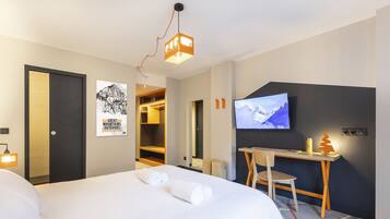 A hotel room with a bed, a desk, a TV, and a poster on the wall.
