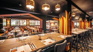 A modern restaurant with multiple dining tables, overhead hanging lights, and a view of the outdoors through large windows. - Base Camp Lodge - Albertville (Albertville)