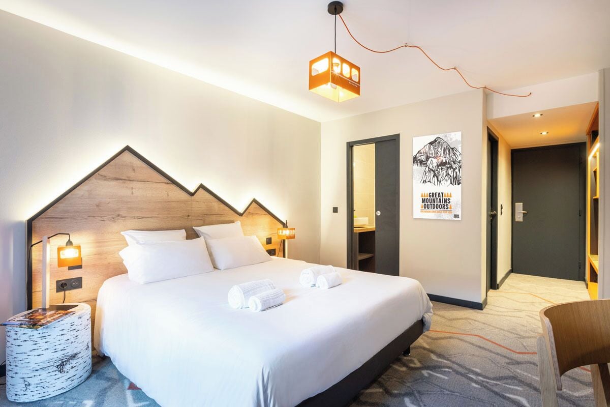 Una camera d'albergo con un letto grande, due comodini con lampade, un tavolino rotondo e un quadro appeso al muro.
