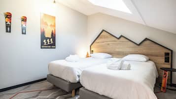 Una habitación de hotel moderna con techo inclinado, dos camas con sábanas blancas, cabeceros de madera y un cartel con motivos de montaña en la pared.