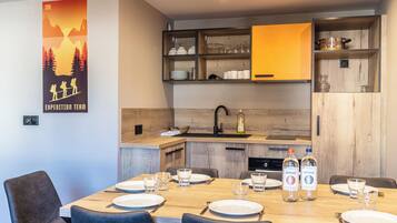 Una cocina moderna con armarios de madera, horno empotrado y comedor con una mesa de madera dispuesta para cuatro.