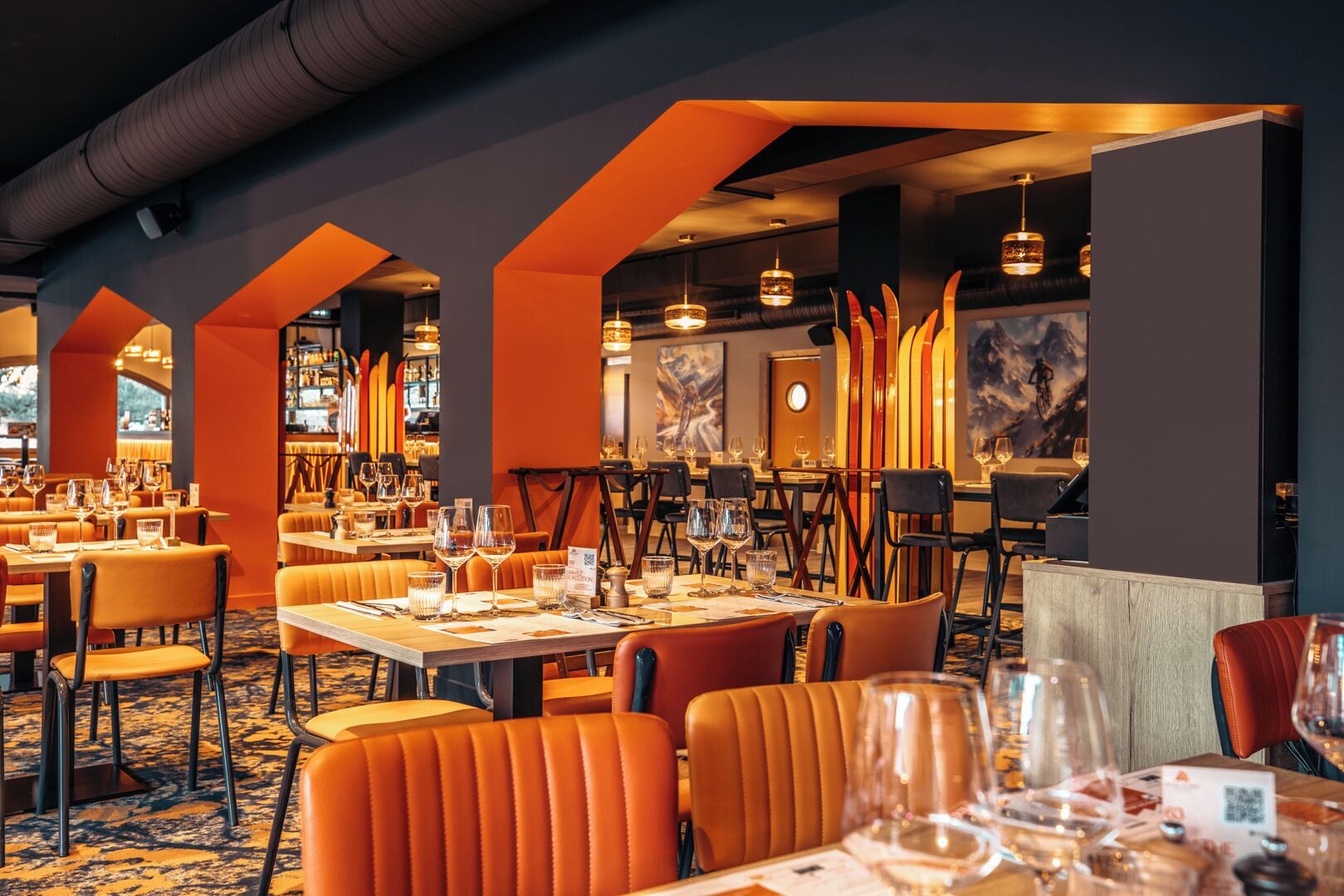 A restaurant with orange upholstered chairs, tables set with wine glasses, and a modern interior design.