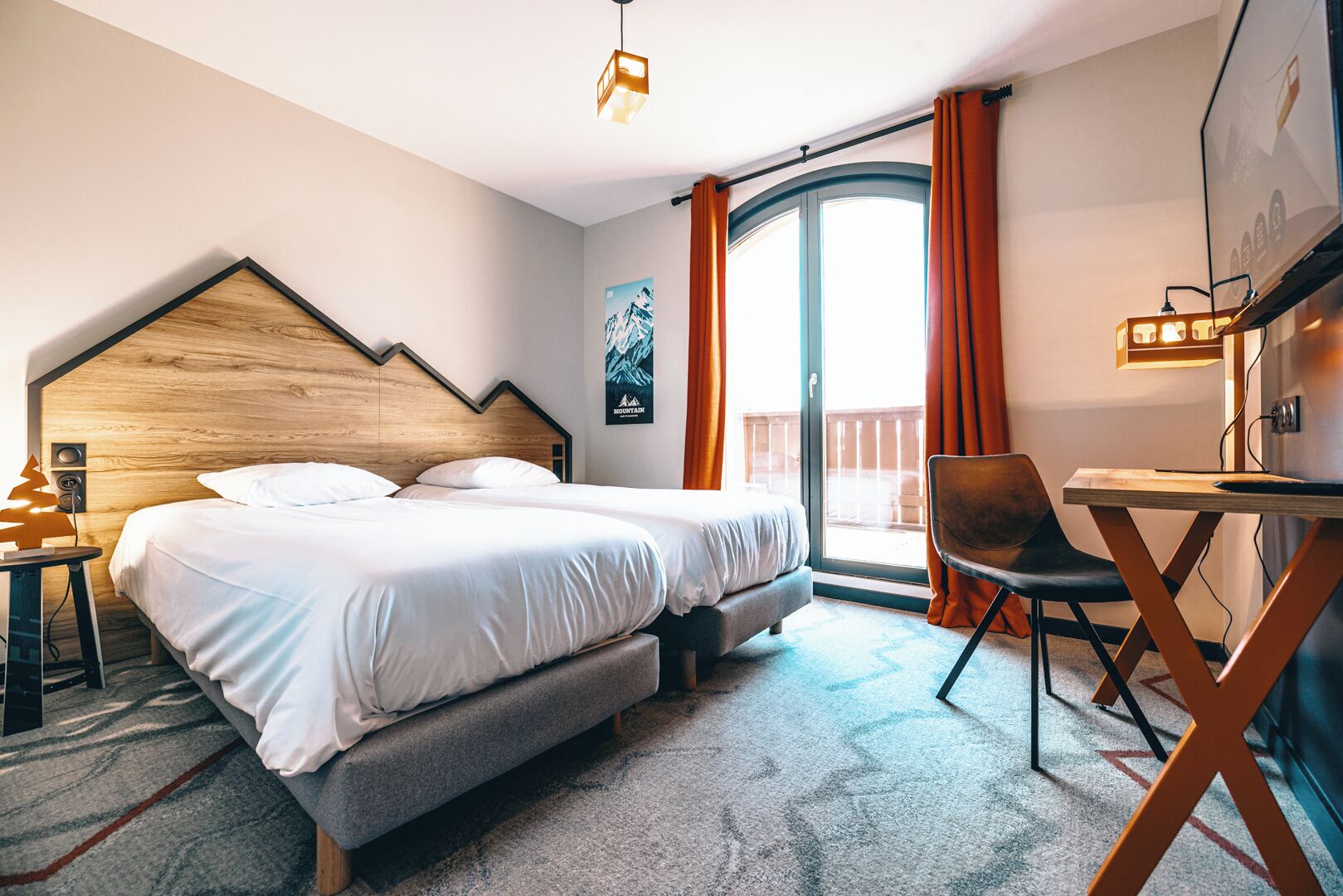 Une chambre d’hôtel équipée d’un lit, d’un bureau, d’une chaise, d’une grande fenêtre avec des rideaux et d’un téléviseur fixé au mur.