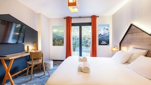 A hotel room with a bed, a desk, a chair, a TV, and two posters on the wall. - Base Camp Lodge - Albertville (Albertville)