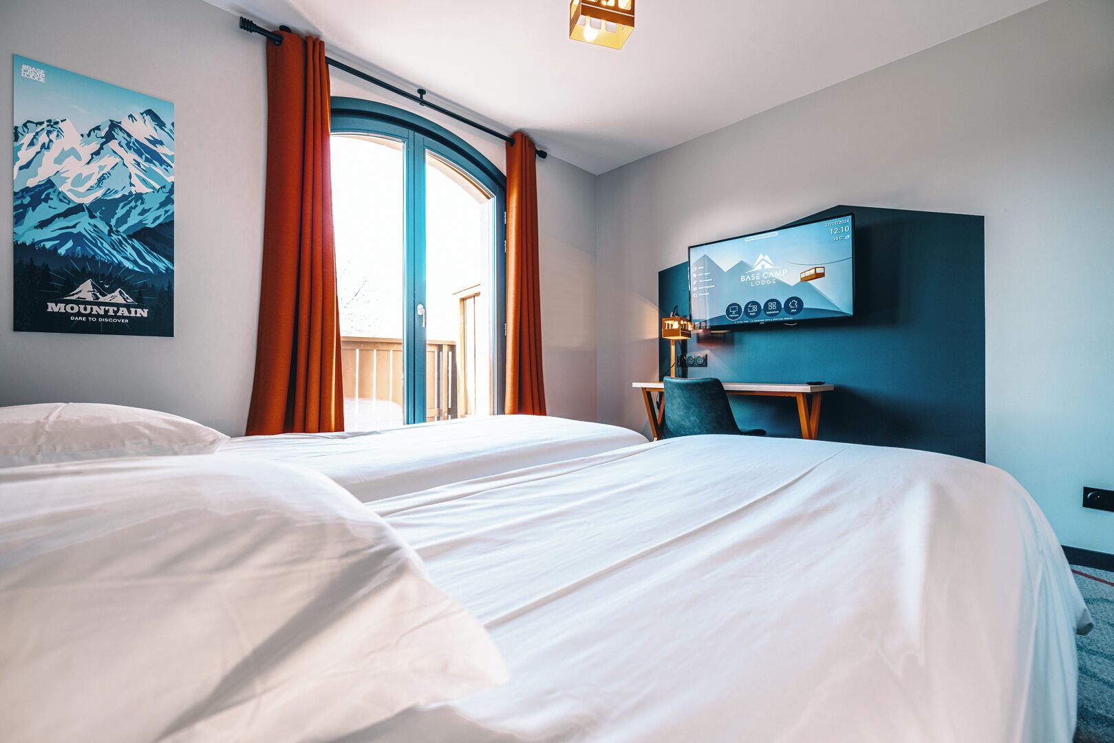 A hotel room with a large bed, a desk, a television, and a window with curtains.