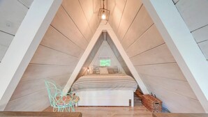 A cozy attic bedroom with a sloped ceiling, a bed with striped bedding, a small chair, and a hanging light fixture.
