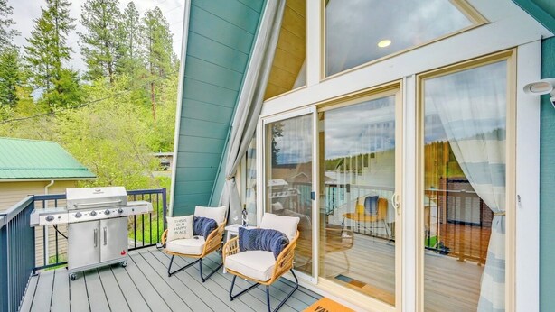 A deck with a grill, two wicker chairs, and a glass door leading to an indoor area.