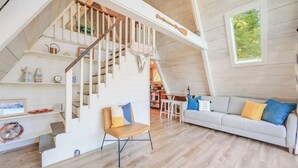 A spacious loft with a wooden staircase, a cozy seating area, and a kitchen in the background.