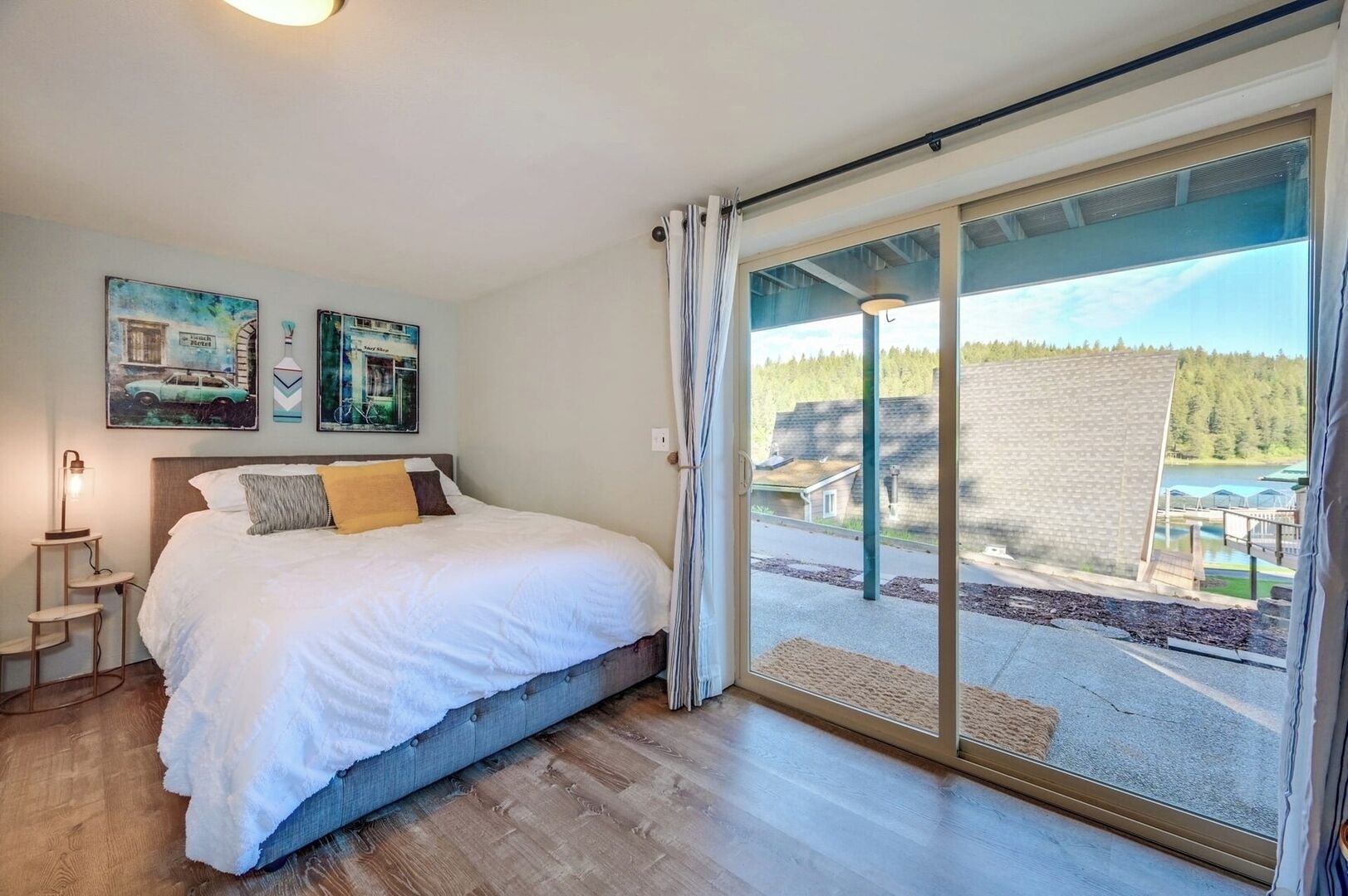 A bedroom with a large bed, a bedside table, and a view of a lake through a sliding glass door.