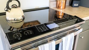A kitchen with a modern induction cooktop, a kettle, and a stainless steel oven. - Vintage Veranda - Ping Pong Table & More! (Fredericksburg)
