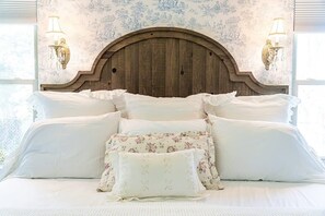 En seng med hvide sengetæpper og puder med blomstermønster, et træhovedgærde og vægmonterede lamper.