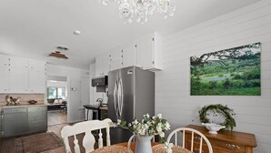 A modern kitchen with white cabinets, a stainless steel refrigerator, and a dining table with woven placemats. - Vintage Veranda - Ping Pong Table & More! (Fredericksburg)