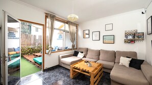 A living room with a sofa, coffee table, and a view of a garden through a sliding door. - KITE & SURF NOMAD HOUSE (Las Palmas de Gran Canaria)
