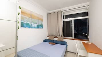 Un dormitorio con cama, escritorio y ventana.