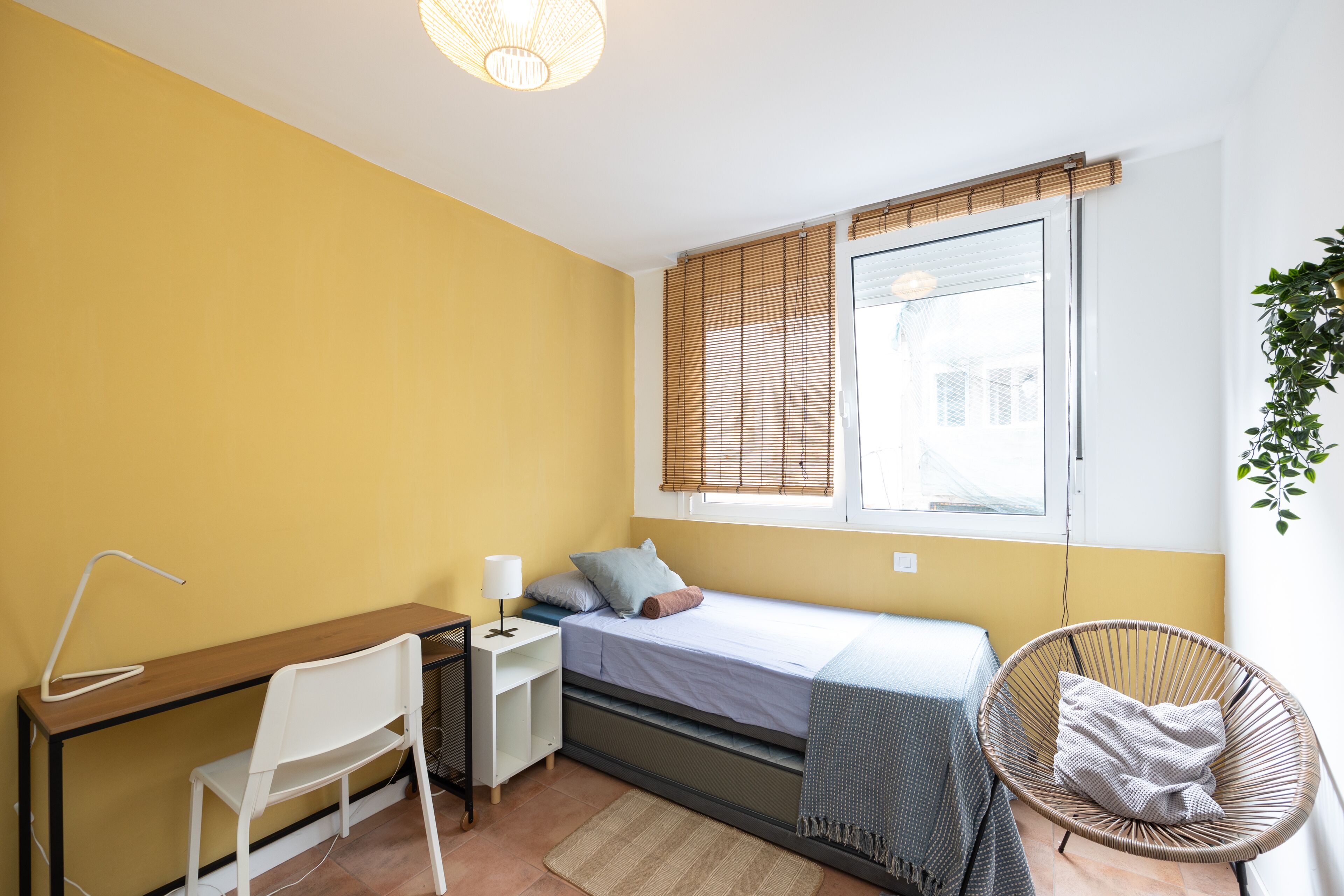Un dormitorio pequeño con cama, mesita de noche, silla y ventana con persianas.