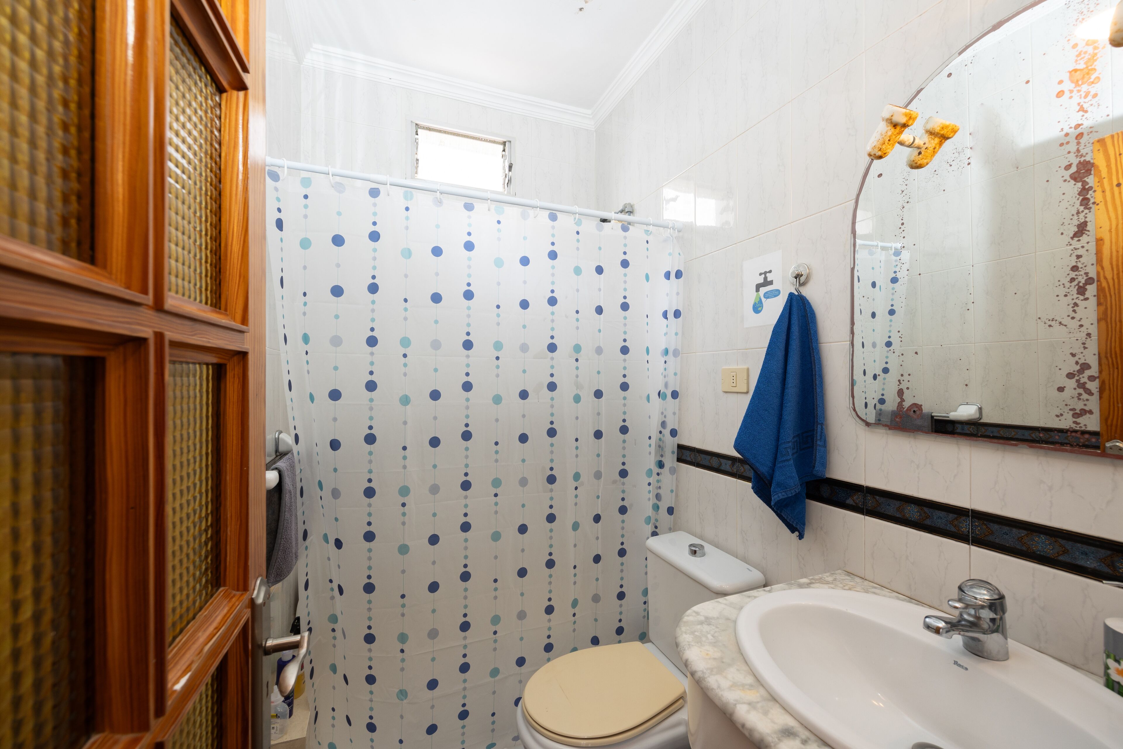 A bathroom with a toilet, sink, shower curtain, and wooden cabinets.