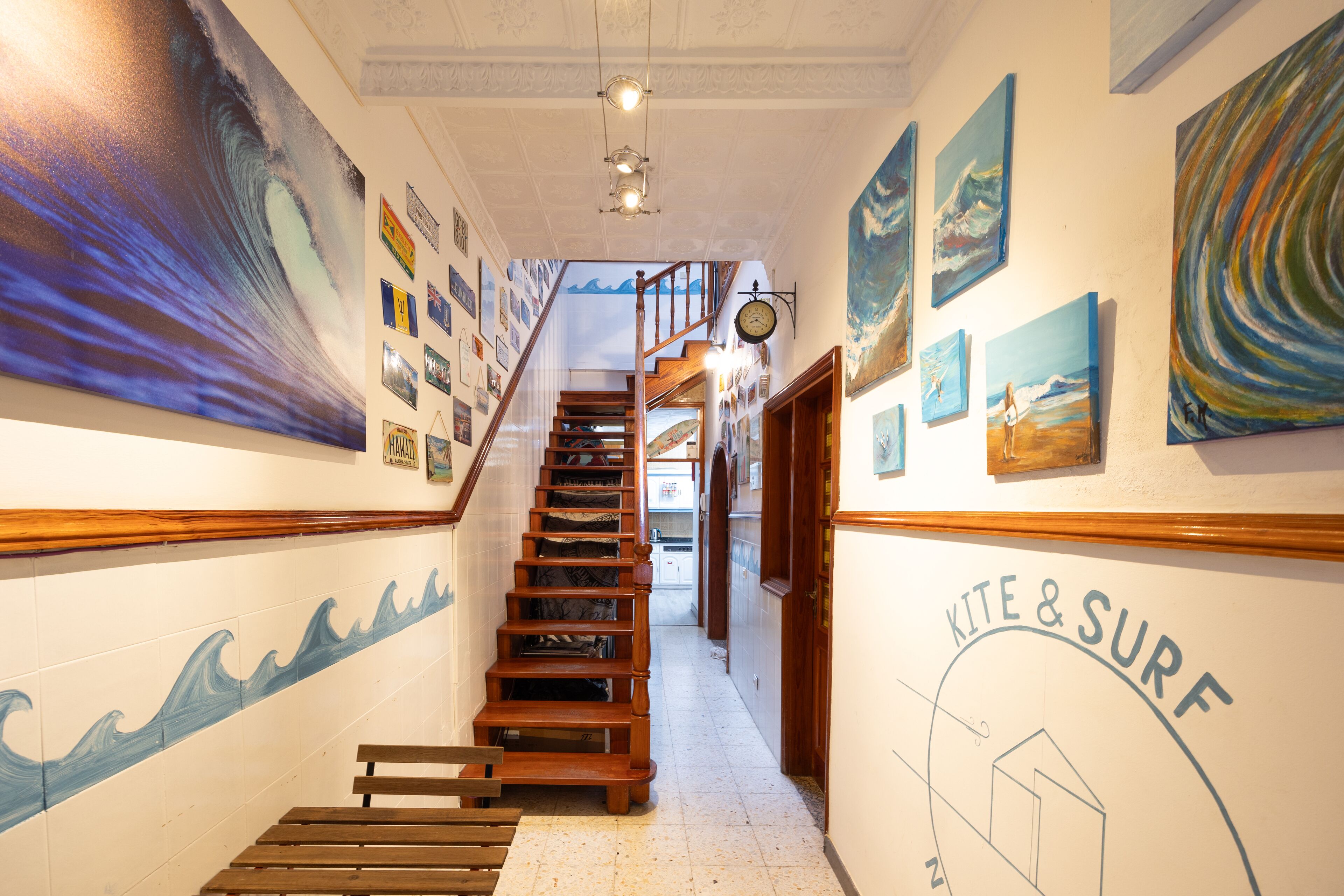 Un pasillo con una escalera de madera, arte mural con motivos de olas y un reloj.
