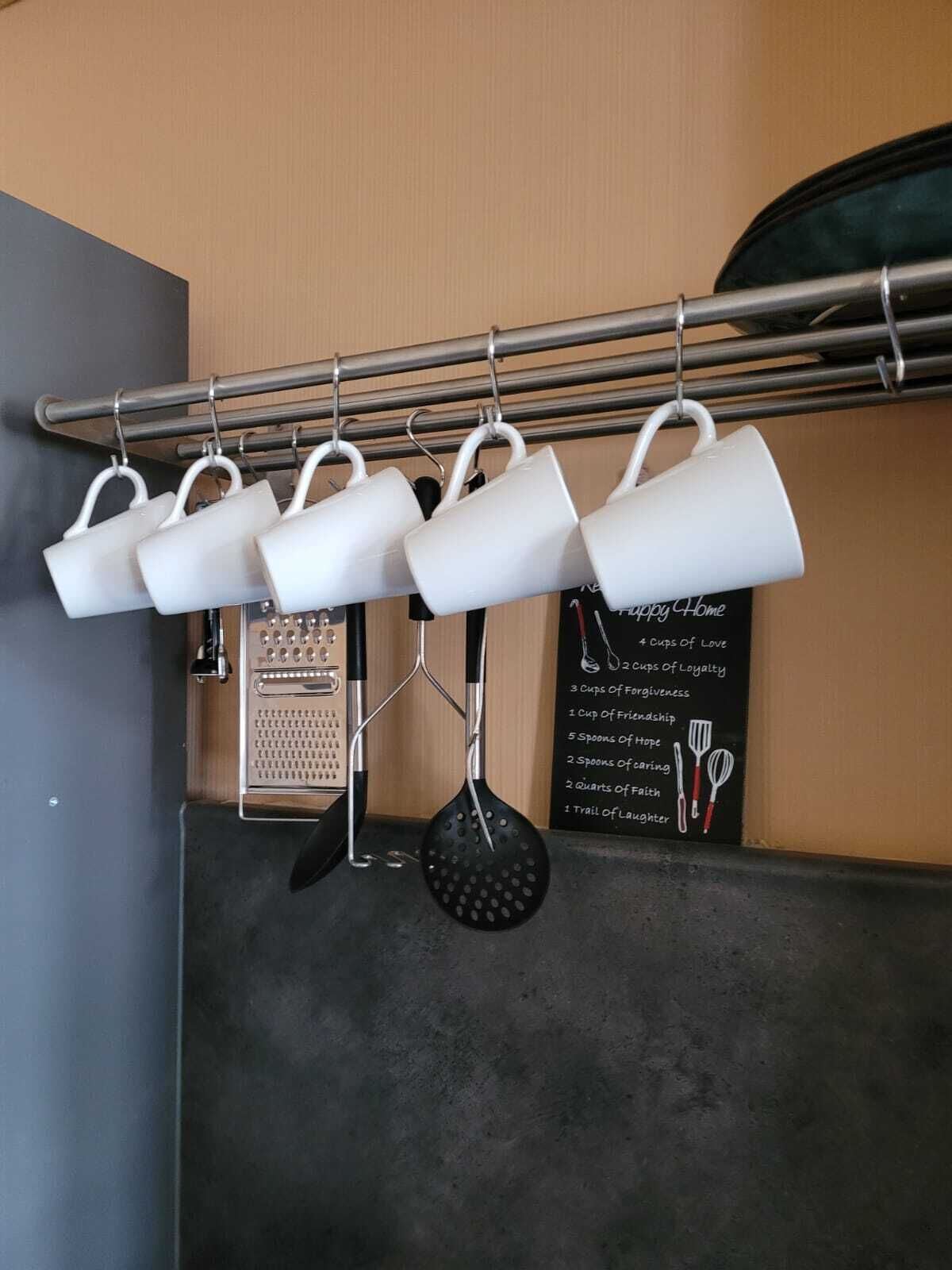 A kitchen with a hanging rack holding white mugs and a black ladle. There is a chalkboard with text and illustrations of kitchen utensils.