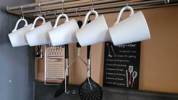 A kitchen with a hanging rack holding white mugs and a black ladle. There is a chalkboard with text and illustrations of kitchen utensils.