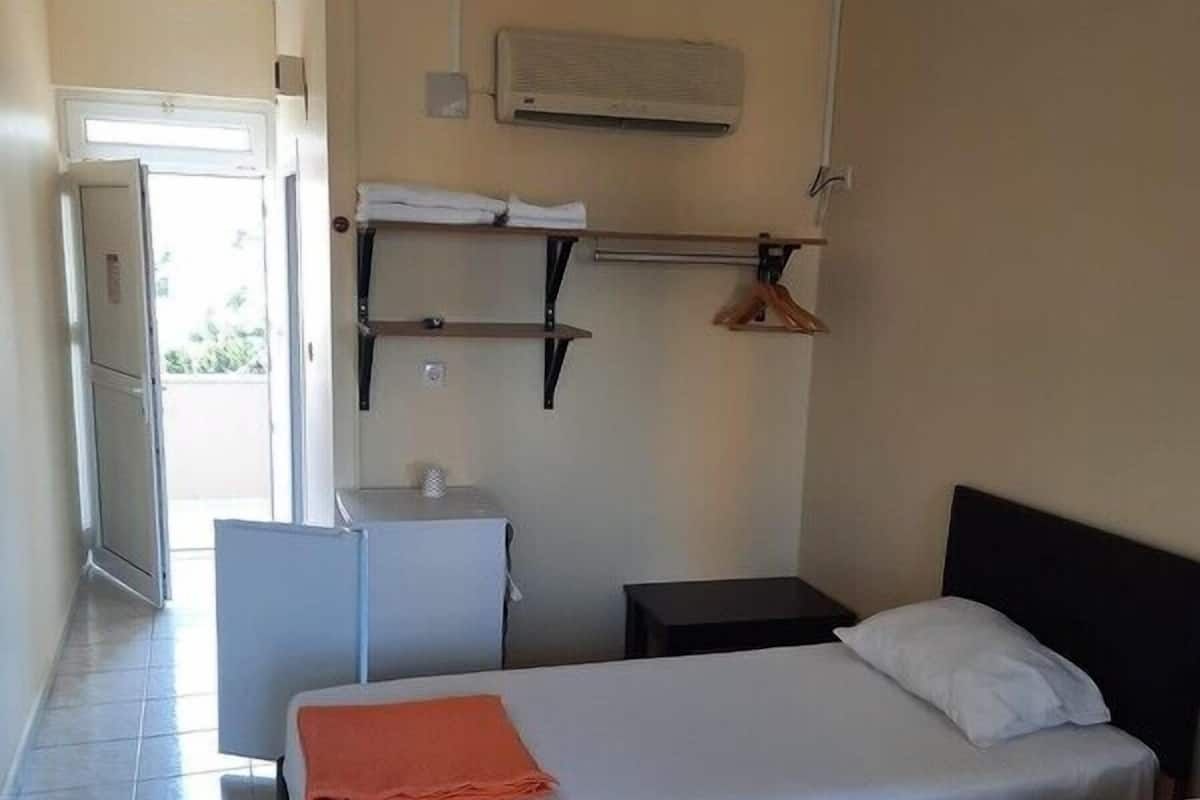 A hotel room with two beds, a small table, a chair, a wardrobe, and a door leading to a balcony.