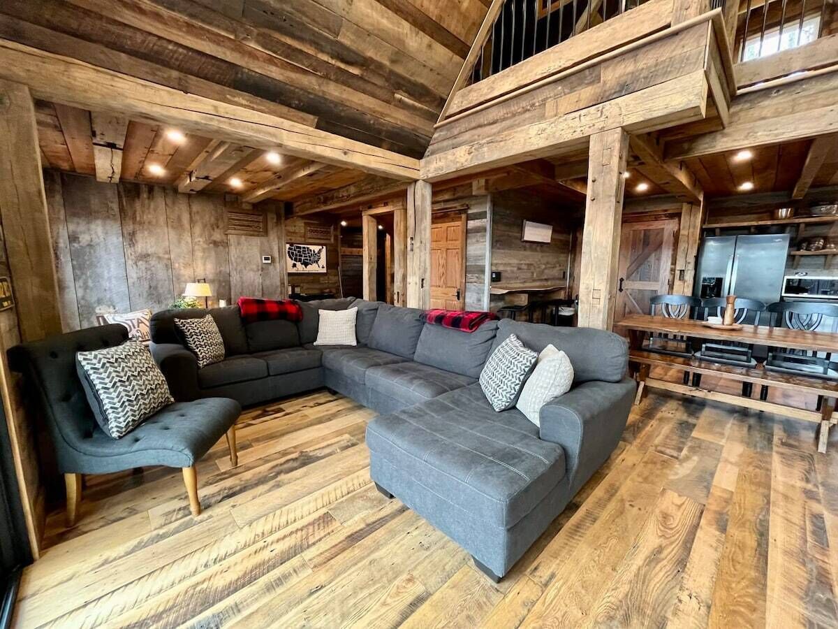 Un interior rústico con un amplio sofá modular en forma de L, suelo de madera y vigas a la vista.