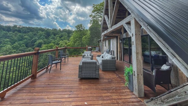 A wooden deck with outdoor furniture, a railing, and a view of a forested hillside. - Estill Oaks - Luxe Mountain View Retreat -Hot Tub - Secluded 80-Acre Escape for 16 Guests (Estill County)