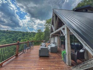 Une terrasse en bois, dotée de mobilier d’extérieur, d’une rambarde et offrant une vue sur une colline boisée.