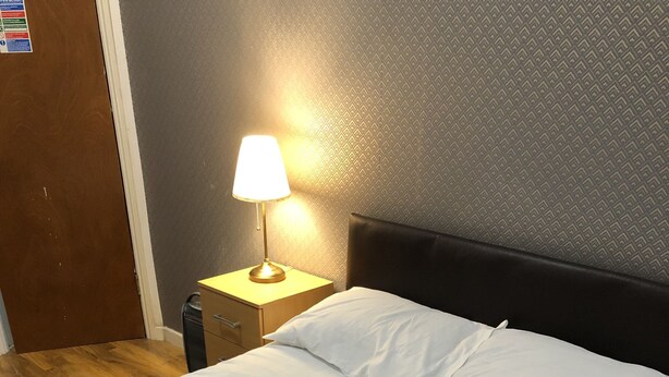 A neatly made bed with white linens, a brown throw blanket, and a bedside lamp on a wooden nightstand. - Suite Overlooking Hyde Park (London)