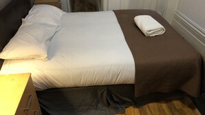 A neatly made bed with white and brown bedding, a wooden floor, and a small bedside table with a lamp. - Suite Overlooking Hyde Park (London)