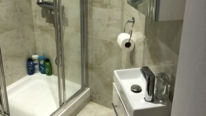 A modern bathroom with a glass-enclosed shower, a white bathtub, and a vanity with a mirror. - Suite Overlooking Hyde Park (London)