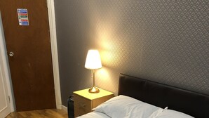 A hotel room with a bed, a nightstand with a lamp, a door with a sign, and a patterned wall. - Suite Overlooking Hyde Park (London)