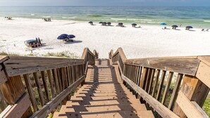 A wooden staircase leading to a beach with white sand and clear blue water.