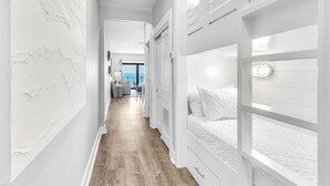 A narrow hallway with bunk beds on one side and a seating area with a view of the sea on the other.