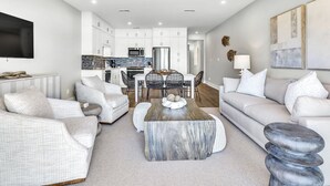 A modern living room with a large coffee table, white sofas, and a kitchen in the background.