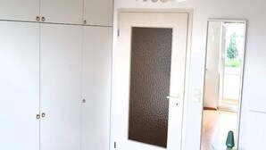 Ein Zimmer mit weißen Schränken, einer strukturierten Tür und Blick auf einen Garten durch eine geöffnete Tür.