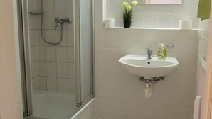 Ein Badezimmer mit einer gläsernen Duschkabine, einem weißen Waschbecken mit Spiegel darüber und einem kleinen Topfpflanzen an der Wand.