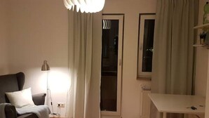 Ein Wohnzimmer mit einer Couch, einer Stehlampe, einem weißen Tisch und einer Schiebeglastür, die auf einen Balkon führt.