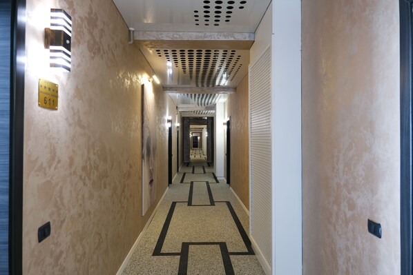 Pasillo de hotel con alfombra estampada, luminarias y una puerta con un número.