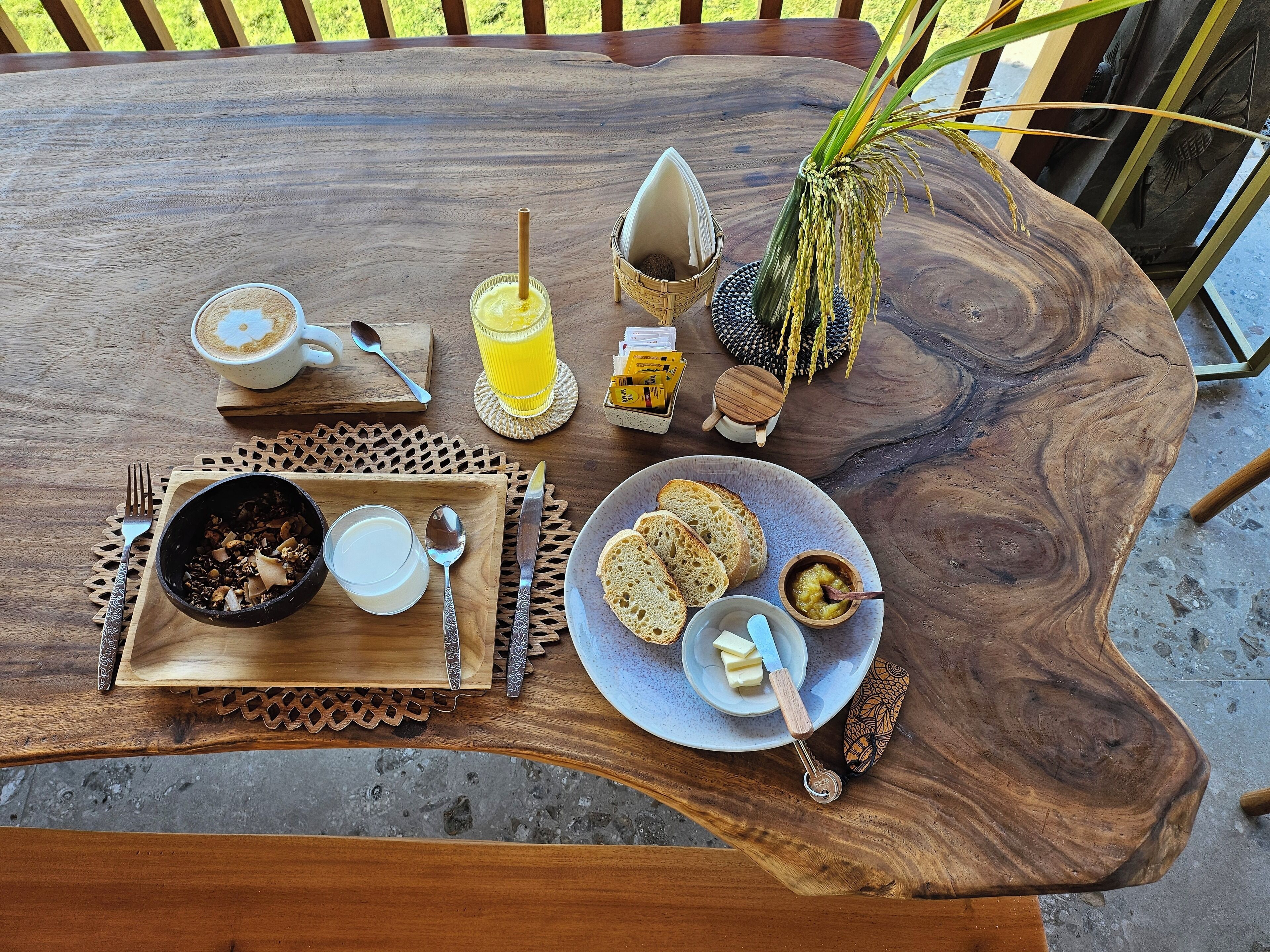Una mesa de madera para comer con elementos de desayuno, como tostadas, mantequilla y un bol de cereales.