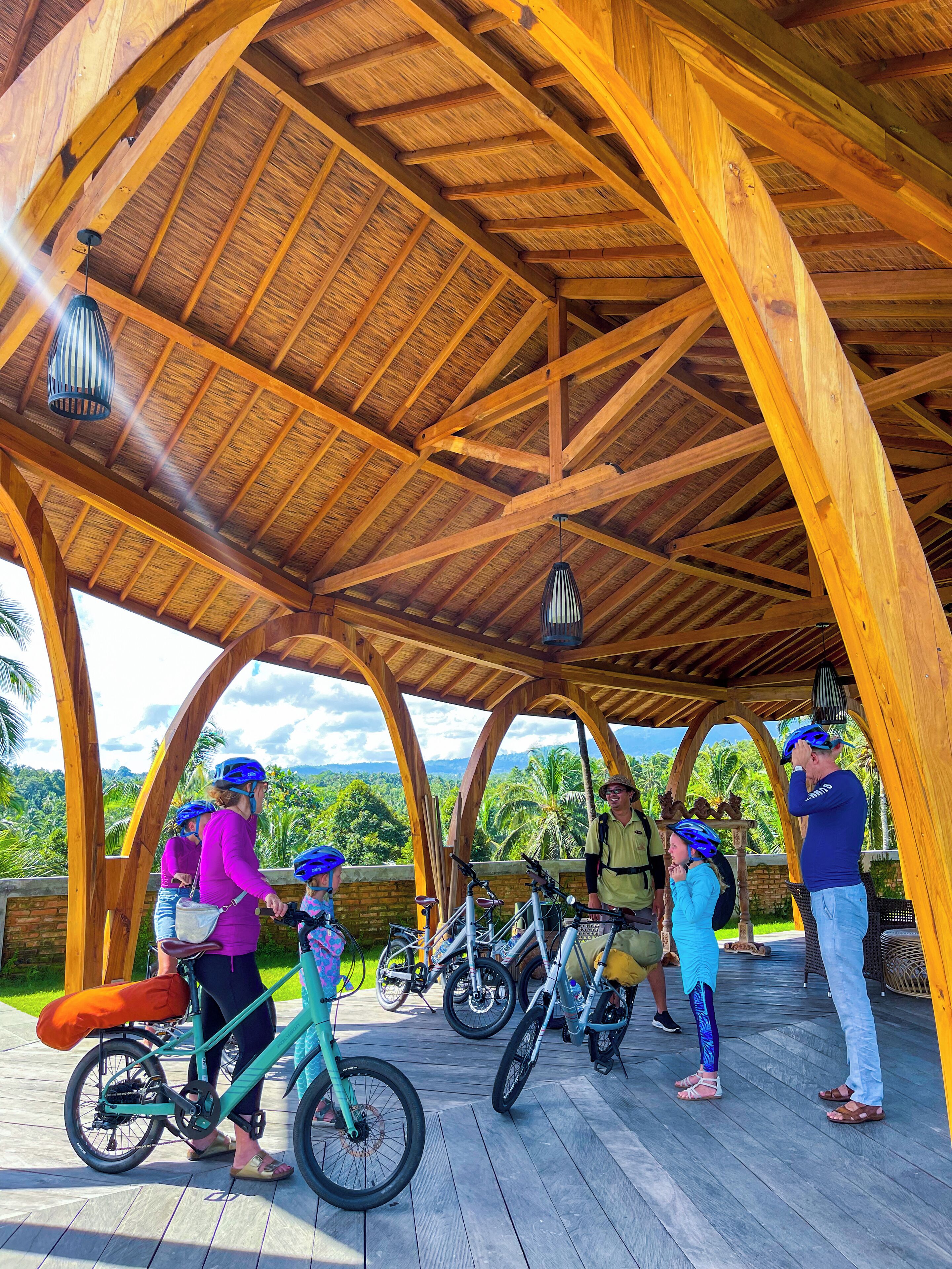 Un pabellón de madera con techo de paja, bicicletas y gente.