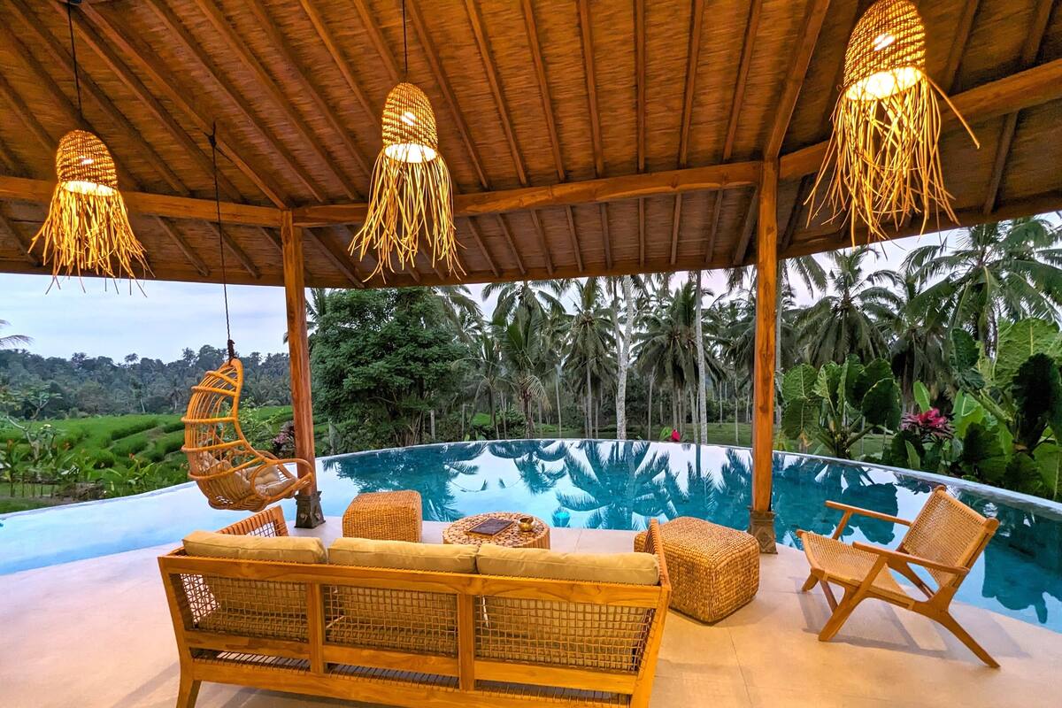 A covered outdoor area with a pool, wicker furniture, and hanging lights.