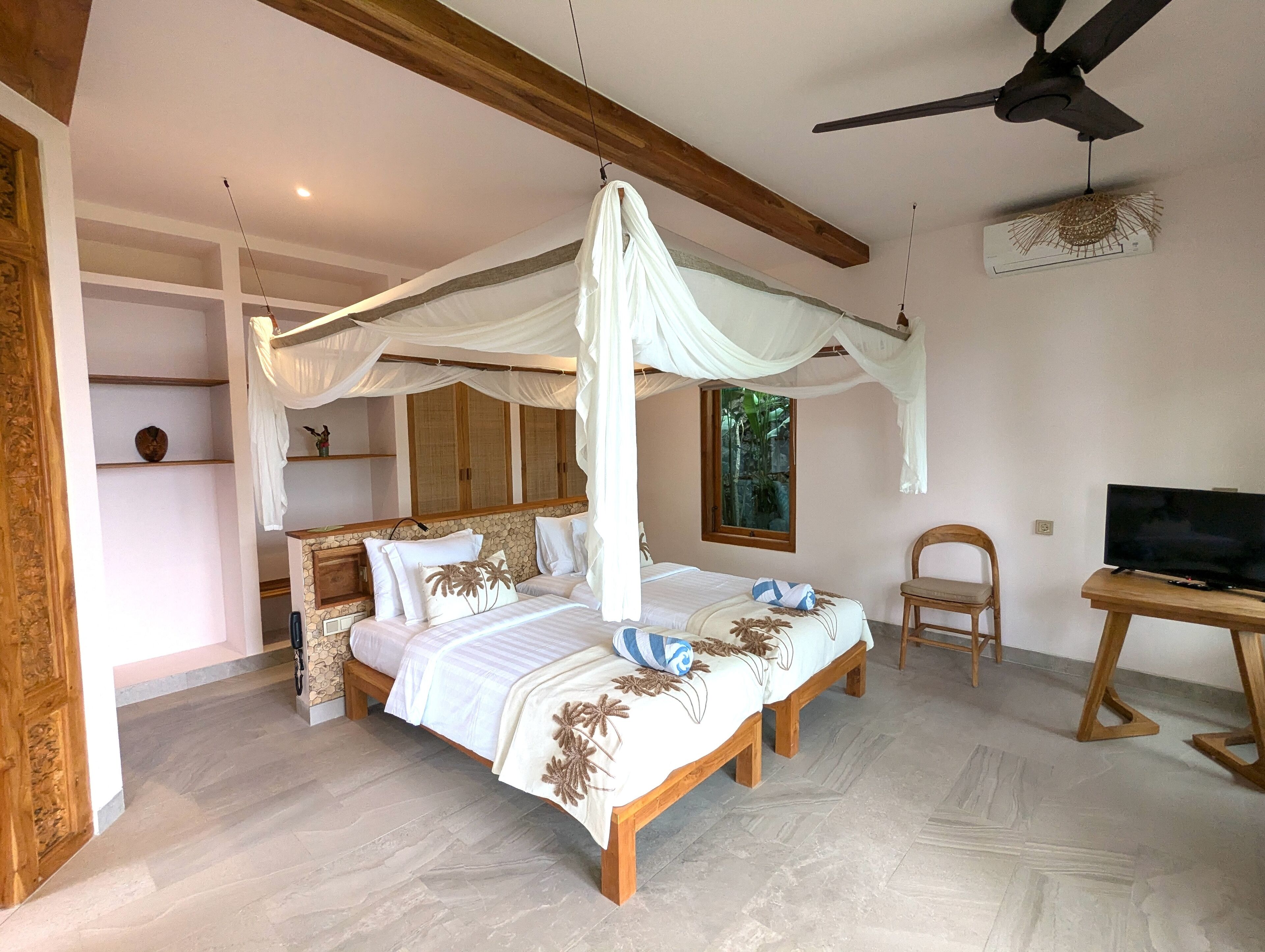 A bedroom with a canopy bed, a ceiling fan, a television, and a stone wall.